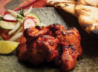 Cooked chicken thigh surrounded by fresh vegetables and naan bread